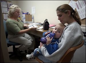 Chris Campbell fills out an assistance application for Bobie Pruett as she comforts her son, Caylib. Ms. Pruett's home and family survived, but her job did not.