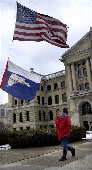 ROV February 4, 2003 - Tom Gerken walks under wind-whipped Lucas County and United States flags flying at half staff on the grounds of the Lucas County Courthouse. The flags are at half staff in honor of the deceased crew of the Space Shuttle Columbia.  Gerken was downtown for jury duty.  Blade photo by Dave Zapotosky