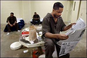 Jermaine Edwards, left, and Antwuan Lawson are seated on their cots as Tony Sanders reads a paper.