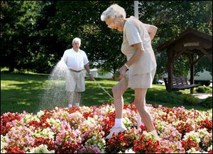 Margaret Hayes tiptoes through the flowers as her husband, George, waters the blooms in the bed in Pray Park in Waterville.