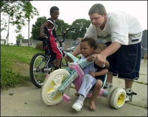 Monte Miller, 8, watches as Corey Corbin helps steer Heaven Baker, 3, and her brother, B.J., 2, near their homes on Broadway in South Toledo. Corey, 14, was keeping tabs on the younger kids yesterday as they played outside. Children may be confined to indoor play today, as forecasters are calling for rain.