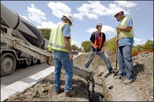 Don Woodward, Tim Heudecker, and John Ezell pour concrete over a conduit along the side of East Wooster Street.