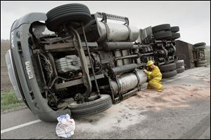 CTY route6wreck 01 - Grand Rapids Firefighter John Berry, checks the semi-truck that overturned on SR 6, south of Grand Rapids, for more leaks in the gas tank area forter spreading absorbant material on the road. 04/27/05. The Blade/Allan Detrich