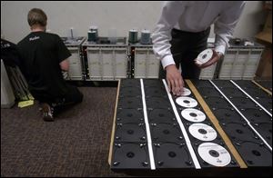 Crew members burn CDs of the group's performance and place finished copies into cases for sale to concert-goers.