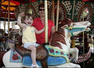 Emma Sullivan, 2, with her grandmother, Lynn Sullivan of Maumee, waves to her grandfather while she rides the merry-go-round at the Wood County Fair.
