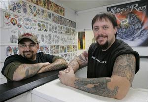 Ron 'Ram' Lee, left, and the Rev. Brian Krabach own Revelation Tattoos in West Toledo. The two artists were drawn together by their faith and a mutual love of tattoos.