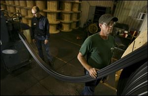 Larry Wilson, left, and Ray Clark, feed material from an extrusion line onto a large wooden spool.