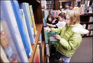 Mackenzie Hall, 11, of Wauseon, foreground, and Taylor Posey, 11, and his sister, Elisabeth, 7, of Delta, check out the children's offerings at the Wauseon Public Library. 