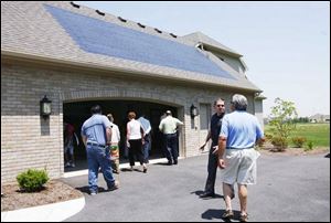 Frank Kozak and Keith Haddad, foreground from left, discuss the solar shingles on the home as others enter it.
