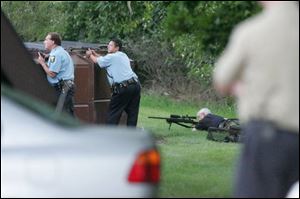 Officers of the Toledo Police Department and a sniper on the grass keep their eyes on an apartment at Oak Hill Apartments on Holland-Sylvania Road in which a man kept authorities at bay for four hours. Authorities found a woman dead in the apartment after he surrendered.