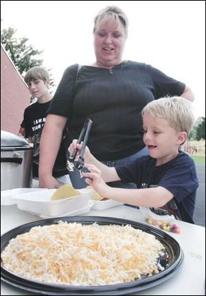 Andy Lenhart, 7, shows his mom Debbie how high a mountain of shredded cheese he can put on his taco at the tailgate party in the back playground at Wayne Trail Elementary School in Maumee. Afterward, participants walked to the Maumee High School football field to watch the Panthers  game against Bowsher.