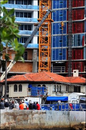 Construction workers stand near where a crane section dropped at a high-rise condominium site and fell on top of a home that a contractor used for storage.