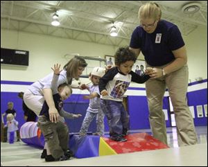 Physical therapist Beth Munoz, at right in foreground, helps Bryson Phillips navigate his way through an obstacle course at the early intervention class for preschoolers at the Blanchard Valley Center in Findlay. 