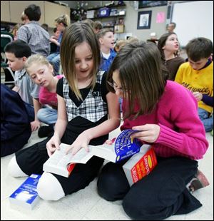 Madison Warncke, center, and Amber Rudd, right, begin their new books at the beginning. The Maumee Rotary began donating the reference books to local fourth graders in 2006.