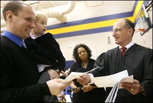 Former United Kingdom citizen Matthew Reynolds, left, holding his son, Nathan, receives his citizenship certificate from Judge Jack Zouhary of the U.S. District Court in Toledo. 