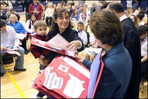 Former Argentine citizen Maria Paula Concepcion Lukac, left, holding her son, Stephan, accepts a welcome gift from Annie Crawford during the naturalization ceremony at DeVeaux Middle School, where 51 people received citizenship. 