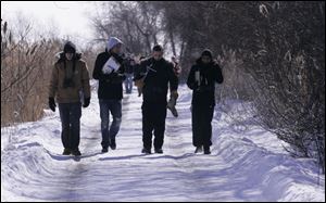 Students walk through the marshland with equipment in tow.