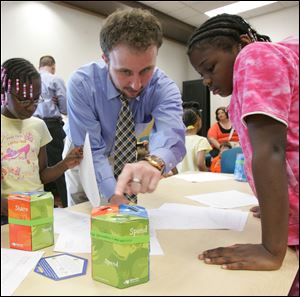 Reed Bennett, an employee with National City Bank, shows Nonye Williams, 8, left, and April Galloway, 10, how to make a Moonjar Moneybox as part of a lesson on how to manage money.