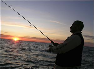 The sun peeks above the horizon providing a backdrop for Toledoan Jim Kaiser as he slowly reels in his lure from the shallows.