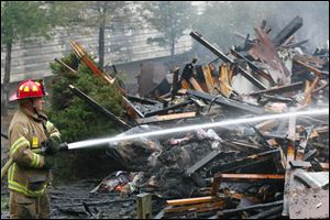 A Springfield Township firefighter pours water on the ruins of Building J at Hidden Cedars. 