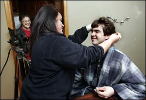 Heather Kalka styles Corey DiNardo's hair as Owens students, working on a video in relationship to their study of Mitch Albom's work, f<0x200A>ilm in the South Toledo home of college instructor Jeremy Meier. Kristen Keller is by the video camera.