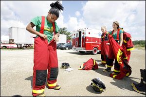 Aalea Robertson, 15, of Toledo, dons firefighting gear while other camp participants look on.