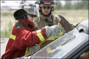 Brooke Moline, 13, of Sylvania, breaks the windshield of a car under the watchful eye of firefighter Tony Caligiuri, of the Northwood Fire Department, at Owens Community College's Center for Emergency Preparedness Heroes Youth Camp Program.