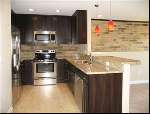 The efficient kitchen is perfectly on-trend with its hues of chocolate and silver, accented by a granite countertop and red pendants.