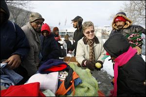 Kerrie Adams, center, hands out fruit as attendees look over stacks of warm clothing being given away by a coalition of community groups. The outdoor event has been held every Saturday for three years.