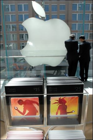 A pair of men talk beside the Apple logo behind a display of iTunes gift cards on the third floor of the Apple store in Boston.