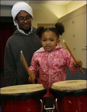 Yahya Travis holds his daughter Asiyah, 3, while she stands on a chair to play the drums last year during 'Bang a Drum' in the Children's Library at the Main Library. 