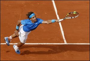 Defending champion Rafael Nadal stretches to return the ball to John Isner during their first round match of the French Ope at Roland Garros.