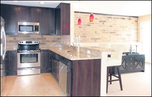 The efficient kitchen is perfectly on-trend with its hues of chocolate and silver, accented by a granite countertop and red pendants.