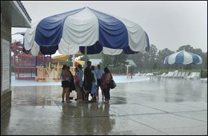 Swimmers huddle under an umbrella at Rolf Park Pool in Maumee as they wait for the thunderstorm to pass through the area.