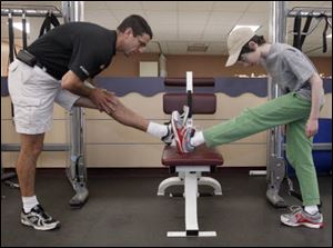 Personal trainer Heath Woodward helps his 15-year-old client , Isaac Ruben, stretch out before their workout at Wildwood Athletic Club.