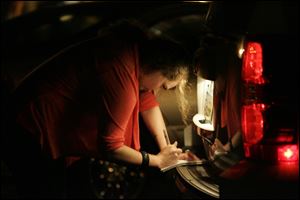 Blade reporter Taylor Dungjen takes notes in the light of a vehicle's license plate bulb while covering members of the gun task force during a summer 