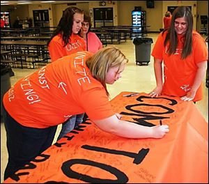 Briel Harper signs the 'Come Together' banner as her eighth-grade classmates Kaleigh Jondro, center, and Oliva Cotterman await their turn.