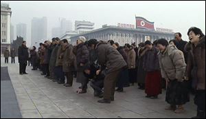 In this image from AP video, a man helps to her feet a woman who collapsed in grief Wednesday as mourners gather to lay flowers in mourning for the late North Korean President Kim Jong Il at the main square in central Pyongyang, North Korea.