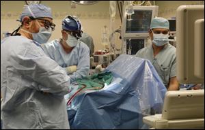 Dr. Khaled El-Syed, left, Dr. Christopher Riordan, and anesthesiologist Mohamad Almasri monitor the functioning of the valve newly implanted in Dr. Todd Monroe.