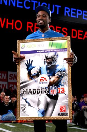 Lions wide receiver Calvin Johnson holds a large print of the cover of the Madden NFL 13 video game. The honor seems to bring some bad luck with it.