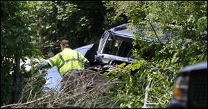 A worker moves brush after a truck today drove off I-475/U.S. 23 and fell into a wooded area along Hill Avenue in Springfield Township.