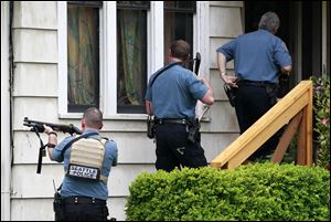 Police approach a house in Seattle's University District near a cafe where a gunman shot five people. Four of them died. Soon after the cafe shooting, a woman was shot to death in downtown Seattle.