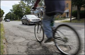 A bicyclist and motorists navigate over cracks and potholes on Bancroft Street near Scottwood Avenue in the Old West End. 