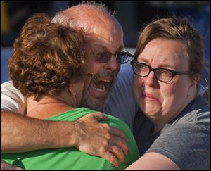 Tom Sullivan, center, embraces family members outside Gateway High School where he has been searching franticly for his son Alex Sullivan who celebrated his 27th birthday by going to see 