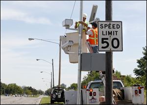 Andy Orshoski of National Light and Power in Sandusky, left, and David Burnham of Redflex Traffic Sysyems, Phoenix, install a speed monitoring camera on the Anthony Wayne Trail in Toledo, Tuesday.  The camera is located between the Toledo Zoo and South Ave.