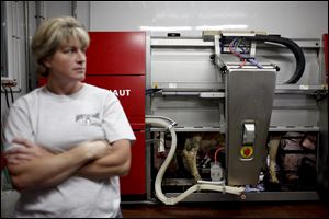 Lisa Groetsch stands to the side on her family farm in Albany, Minn., as the automatic milking system goes to work. The system lures the cow with a treat, scans and cleans its teats, and milks the cow.