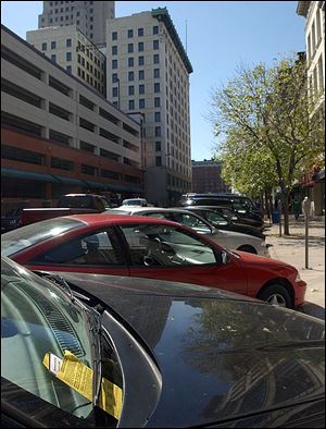 A parking ticket is visible on the windshield of a car parked at a meter on Superior Street in downtown Toledo.