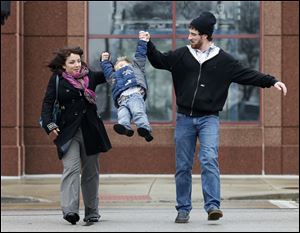 Anita and Rusty Ybarra swing their son Gauge Ybarra, 4, as they cross Summit Street in an unseasonably warm Toledo Tuesday.