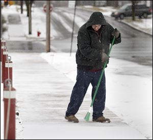 Toledoan Luis Perez sweeps a dusting of snow off a sidewalk near the Hose Sales Direct parking lot at Broadway and Newton streets in Toledo, Ohio. Perez is a janitor at the business.