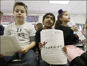 Second graders Anthony Kovacs, 8, left, Nikhil Methi, 6, center, and Adrianna Magers, 8, right, hold autobiographies today with ideas about ways they could help people in their communities.